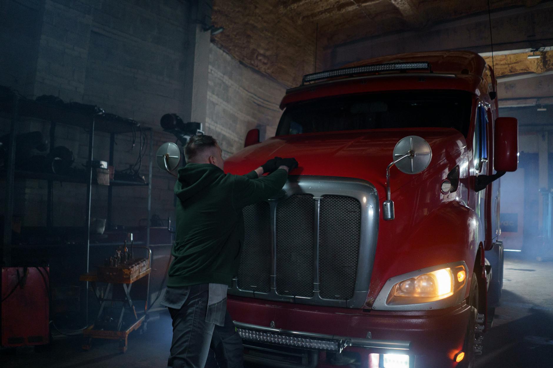 Mechanik w półmroku warsztatu naprawia czerwoną ciężarówkę