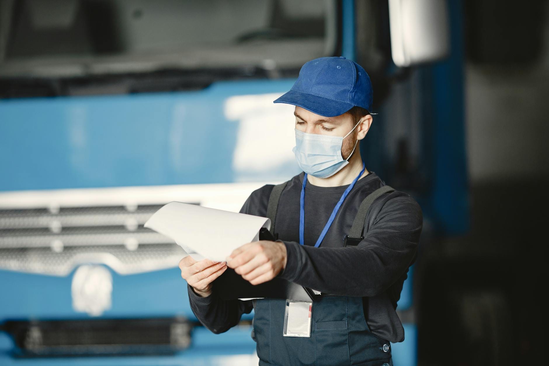 Mechanik w masce i czapce przegląda dokumenty w warsztacie samochodowym