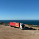 Biały tir z czerwoną naczepą jedzie nadmorską drogą nad Bałtykiem