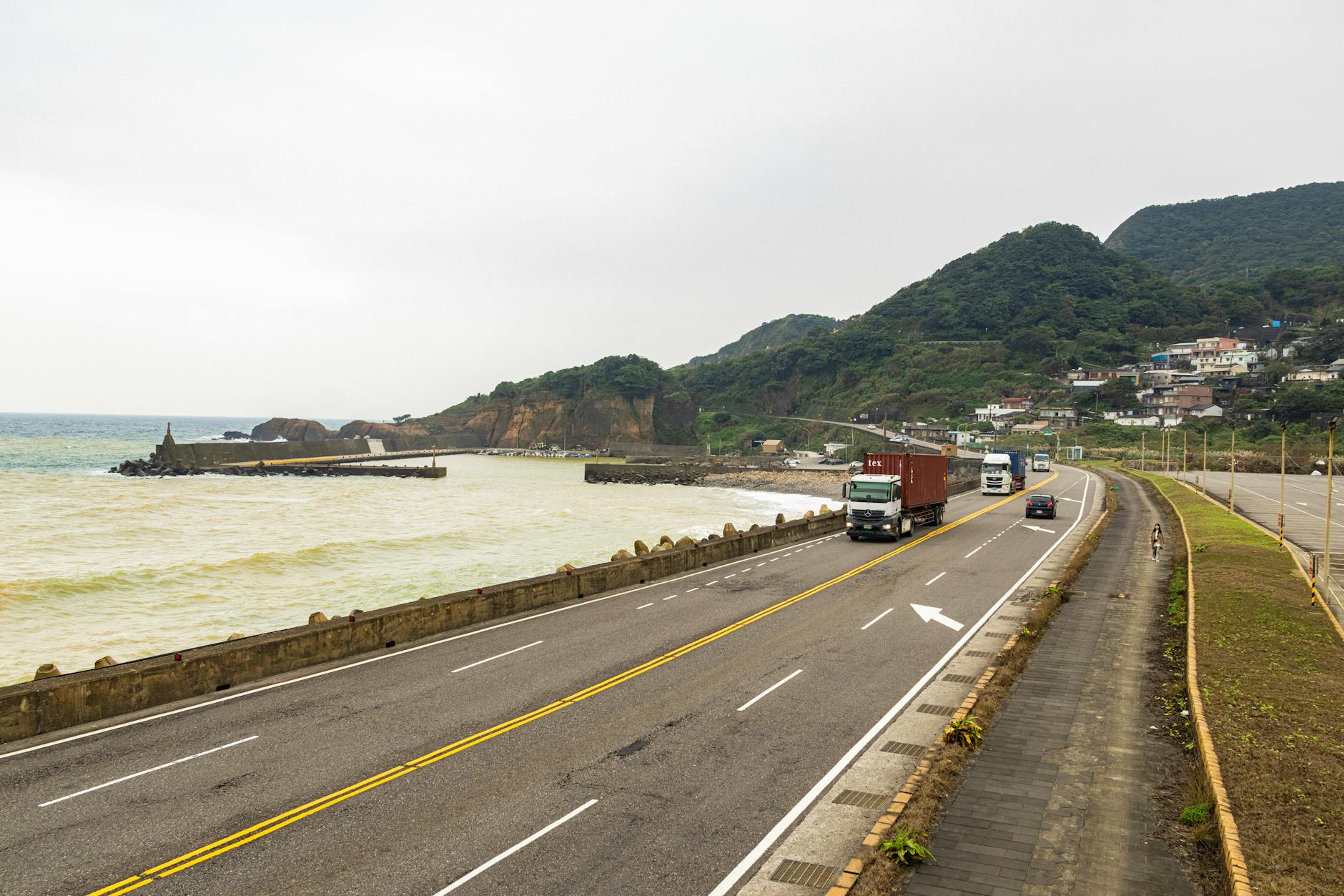 Ciężarówki jadące nadmorską drogą z widokiem na góry i ocean